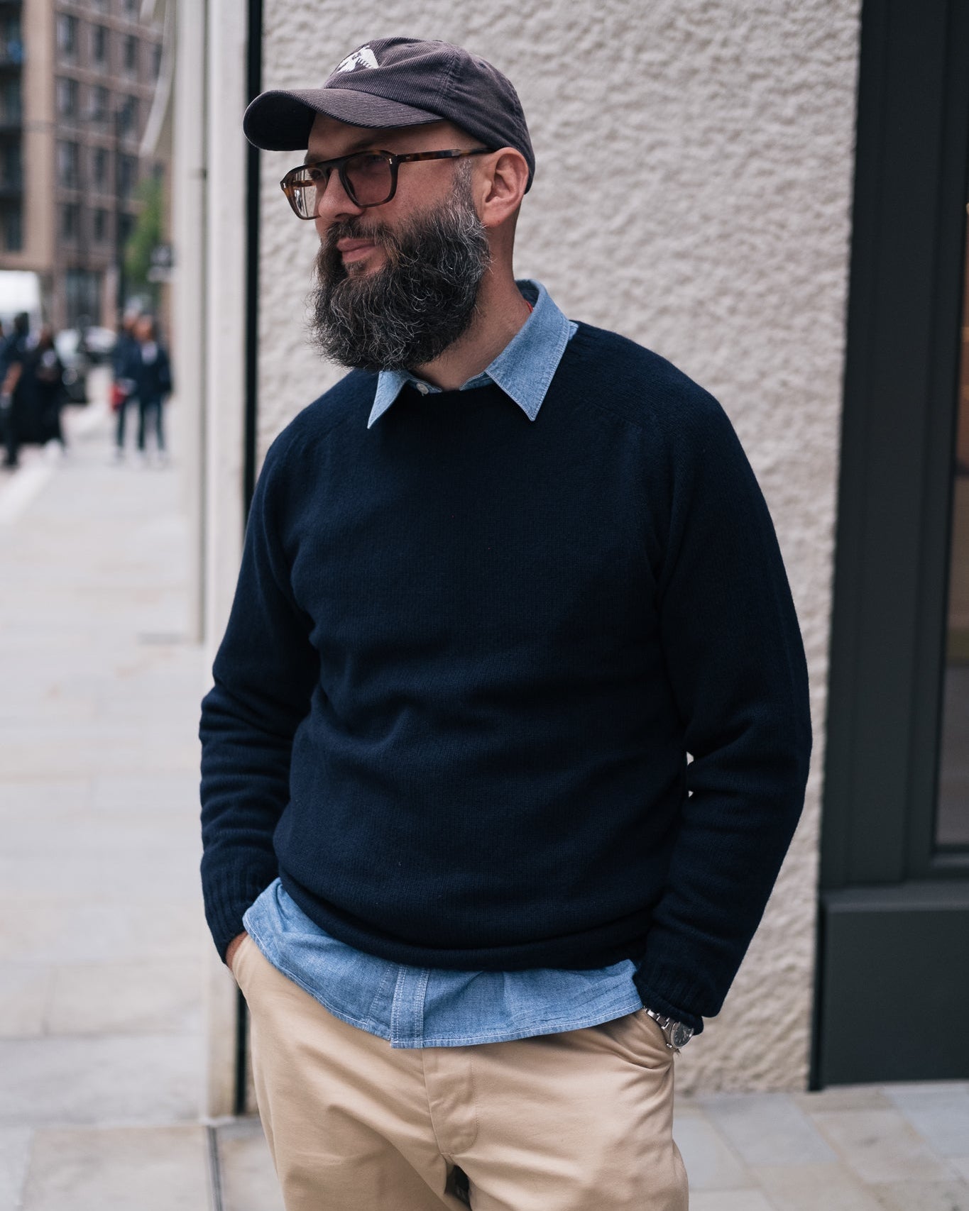 man with beard wears a navy superfine lambswool jumper with a chambray shirt and chinos